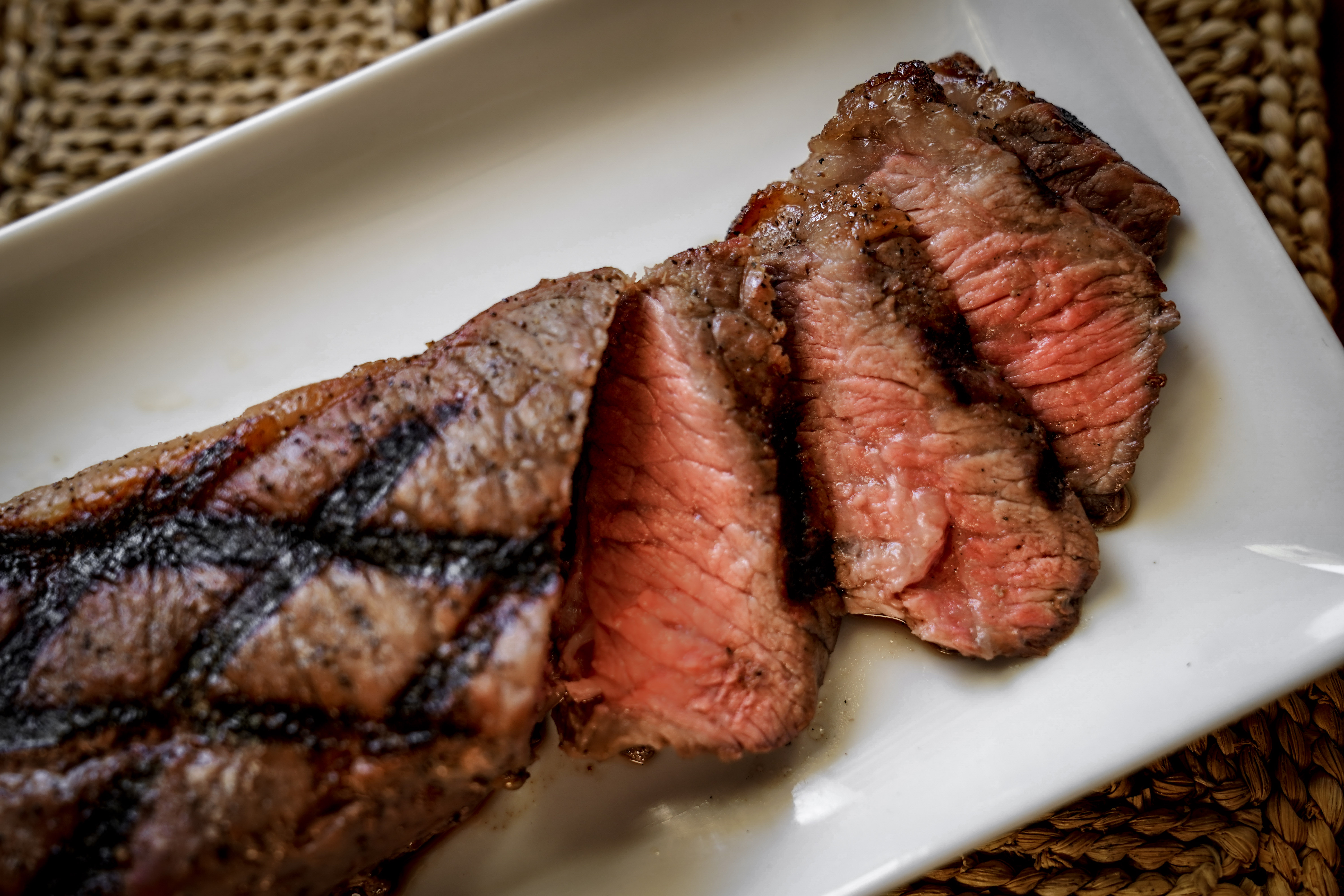 Grilled steak slices with seared marks, served on a white rectangular plate.